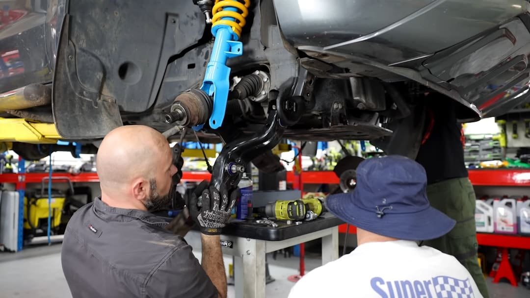 Technicians working on front suspension components with the wheel removed