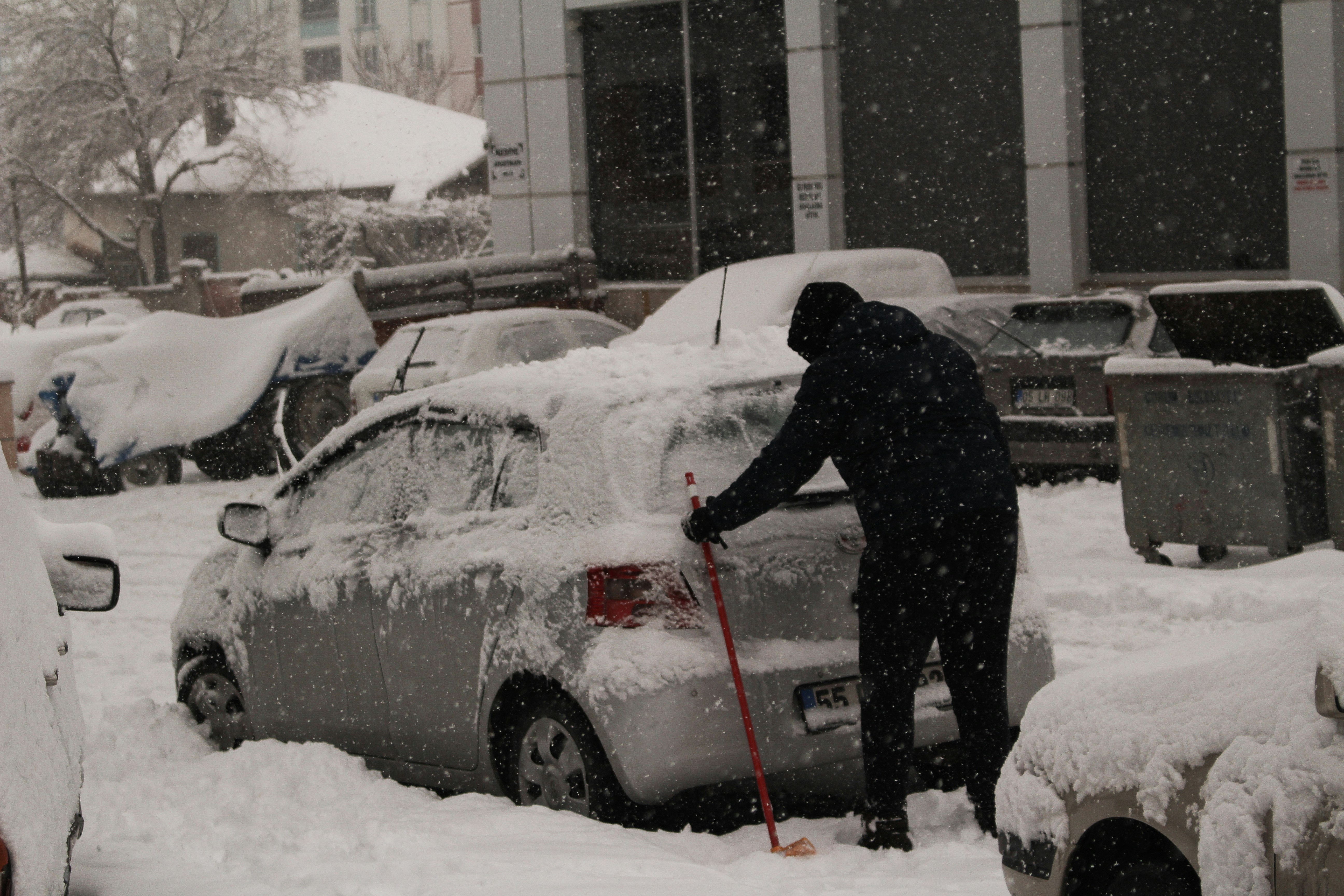 Person cleaning snow off car during Chicago winter - proper winter car preparation and maintenance